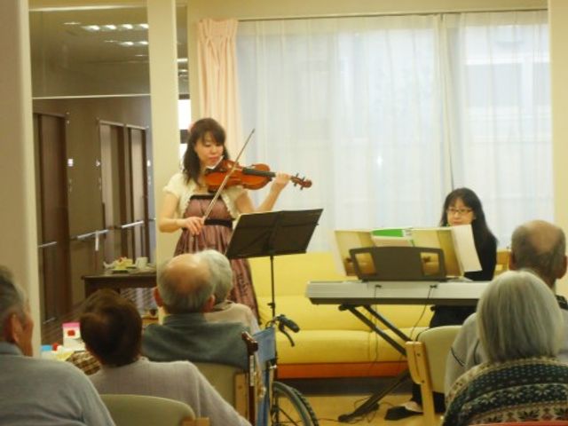バイオリン演奏の多目的室 談話室 バイオリンの生演奏を聞きながら、日々の暮らしに潤いを与える憩いの時間を提供しています。職員もゲストの演奏を介助しながら楽しめる環境が整っています。