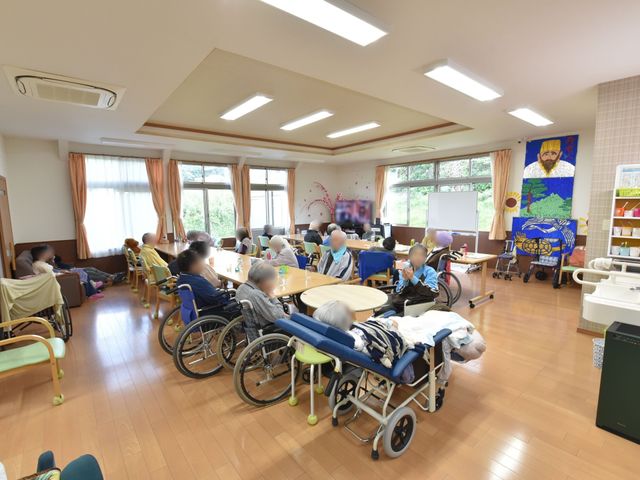 明るい共有スペースの居室 共有スペース ゆとりある居室で利用者様がくつろいでいます。窓からの自然光が、穏やかな雰囲気を醸し出しており、ゆったりとした時間を過ごせる空間です。