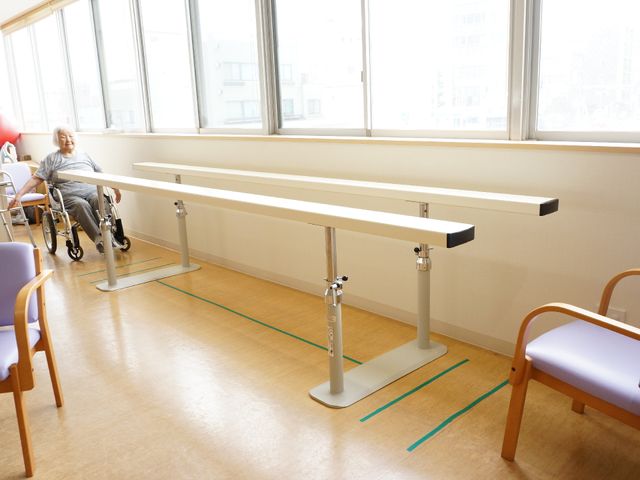 リハビリ室と利用者 平行棒 窓際に明るい光が差し込む訓練室で、安らぎの一時を過ごす様子です。