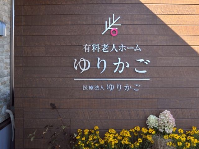 看板の文字と花壇 施設名称 明るい日の光の下、洗練されたデザインの看板がお出迎えします。
