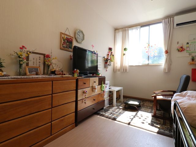 和やかな居室風景 居室 木目調の家具と暖かい光が入る窓が特徴の居室です。日々の安らぎの時間を過ごす空間として、ご利用者に心地よい場所を提供します。