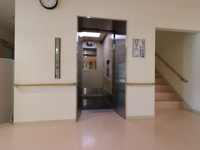 廊下のエレベーターと階段 エレベーターホール このエレベーターは階段と並んで設置されており、利用者の移動をサポート致します。安全に配慮された設計が随所に見られます。
