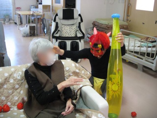 節分行事をお楽しみ中の居室 日常 椅子に座る方が、節分行事で豆まきを楽しんでいます。笑顔で日々の生活に彩りを加える催し物が充実しています。