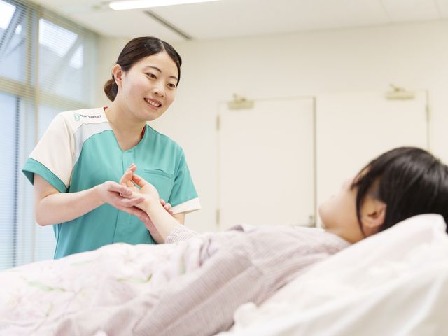 看護師と利用者の様子 居室 明るい空間で、看護師が利用者に笑顔で対応しています。居心地の良い環境が整っています。
