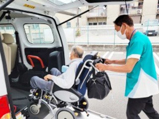 車椅子での乗車補助をする場面 スタッフイメージ 職員が車椅子の方を車に安全に乗せる様子です。サポートが行き届いた環境が整っています。