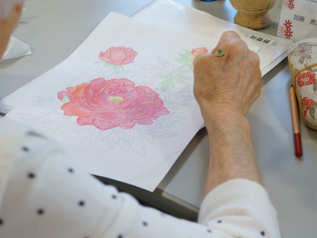 花の絵を描いている手 訓練室 様々な活動が楽しめる多目的室で、手に取った色鉛筆で丹精込めて花の絵を描く光景です。創造性を発揮しながら心豊かな時間を過ごせる場所となっています。
