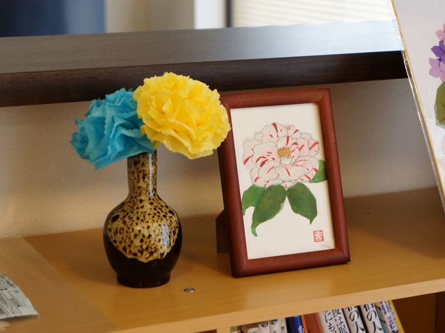 花と絵が飾られた棚 製作した作品の展示 手作り感のあふれる花と絵画が並ぶ棚の上です。このような温かみのある工夫が随所に見受けられる空間で、ご利用者の日々が豊かになります。