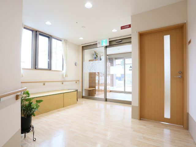 エントランスの明るい空間 玄関 手すりとベンチが備わり、休憩しながら外の景色も楽しめる快適な入口です。デイサービスの日々が、この明るく開放的な場所から始まります。