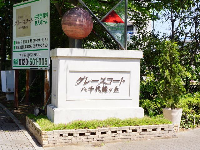 看板の前の緑豊かな場所 看板 木々に囲まれた看板が施設の顔となり、明るく穏やかな雰囲気を感じさせます。このような環境での仕事に関心があれば、一度検討してみてはいかがでしょうか。