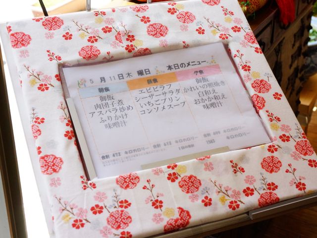 花柄が映える掲示物 メニュー表 和風の柄がある掲示板が目に留まります。利用者様の彩り豊かな生活をサポートする様子が伝わります。