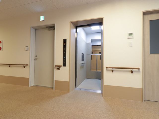 廊下と扉の様子 エレベーター 手すりが設置された廊下は、明るく清潔感があり、安全な移動をサポートしています。扉のデザインも無駄がなく使いやすそうです。