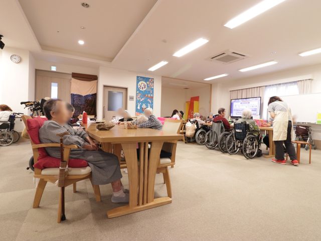 共用スペースの日常風景 食堂 椅子に座ってくつろぐ方々と食事の準備をするスタッフが見え、日々の生活が和やかに行われている食堂です。