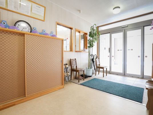 玄関はガラスの自動ドアで、開放感がある。入ってすぐ右に傘立てがある。大きな下駄箱が設置された壁の上に額と時計が掛かっている。