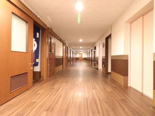 清潔感のある廊下 男湯女湯 木目調デザインの床や壁が暖かみを感じさせ、明るく広々とした通路が特徴です。