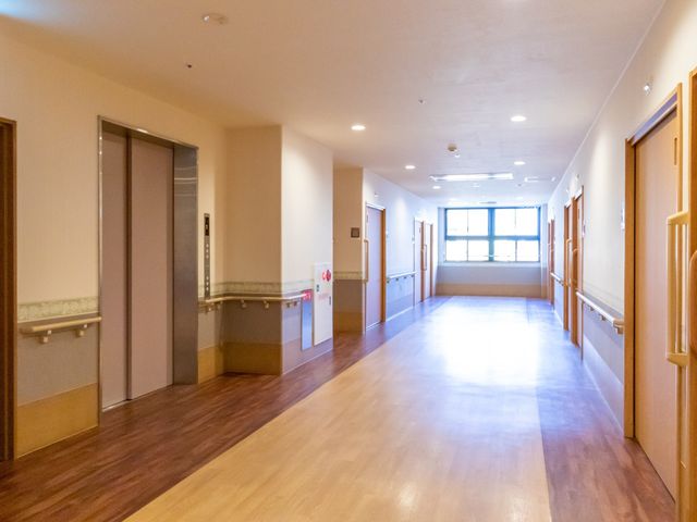 明るく広い廊下 通路 広々とした廊下は天井が高く、柔らかな光が差し込んでいます。壁には手すりが取り付けられ、サポートが必要な方も安心して歩ける設計になっています。