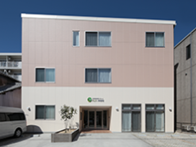 3階建ての施設外観 外観   落ち着いた色合いの3階建ての建物で、正面に出入口があります。駐車スペースも見えており、就業時の出入りがしやすそうです。