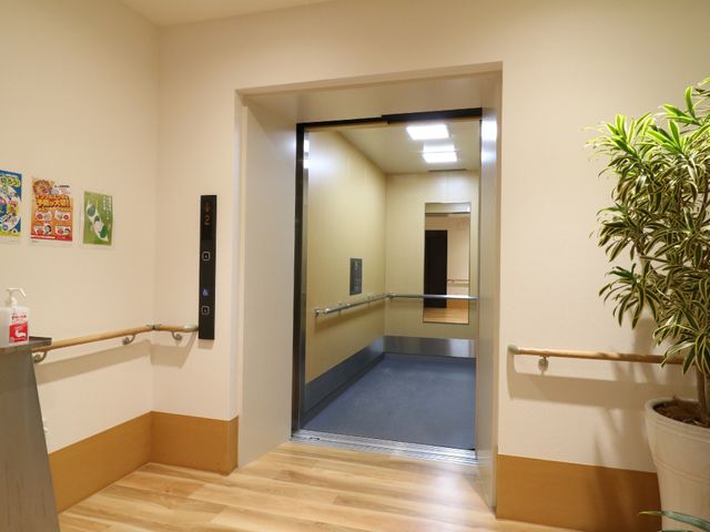 手すり付きエレベーター入口 エレベーター 広々としたエレベーター前は明るく、手すりが整備されています。壁には掲示物もあり、情報共有の一環となっています。