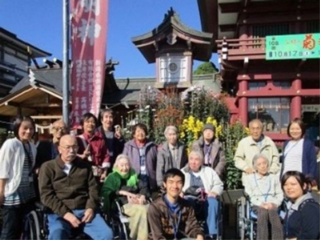 集合する笑顔の人々 明神様へお参り 心温まる笑顔であふれるスタッフと利用者様の集合シーンです。和やかな雰囲気の中で、仕事にもやりがいを感じていただけることでしょう。