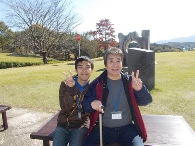 笑顔でポーズを取る利用者 外出時 ゆったりとした中庭で、利用者が穏やかな時間を過ごしている様子です。日差しを浴びながら、外の空気を感じる瞬間をお楽しみいただけます。