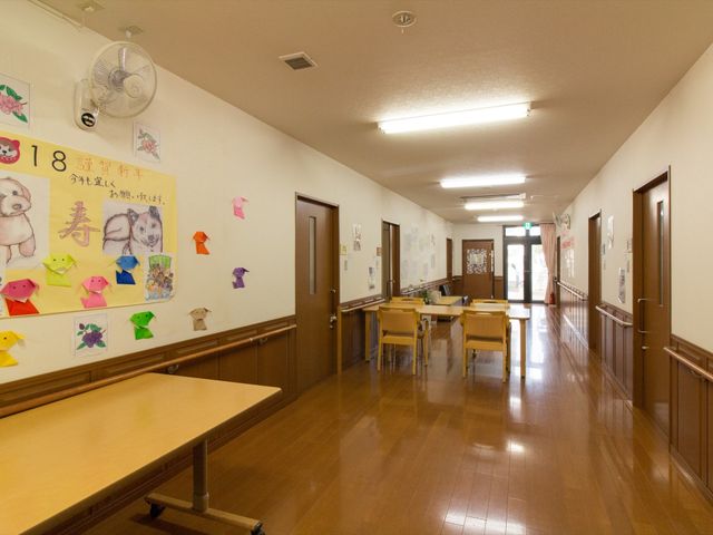 廊下にあるテーブルと椅子 談話スペース ゆったりとした廊下にはテーブルと椅子が配置されており、休憩や交流のひとときを提供しています。壁には手作りの飾りがあって温もりが感じられます。