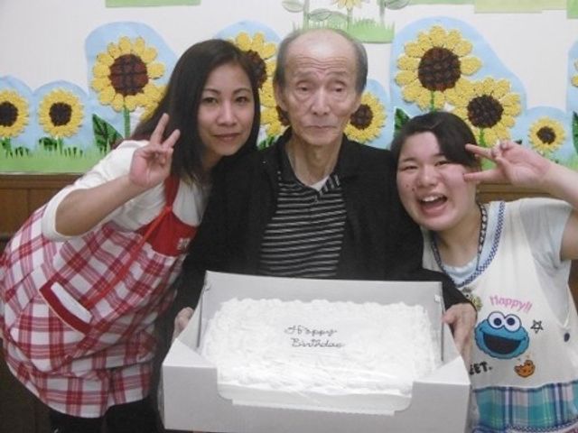 お祝いケーキと笑顔の人々 お誕生日 スタッフが入居者の誕生日を祝福し、共に楽しい時を過ごしています。温かい雰囲気で職場体験をしてみませんか。