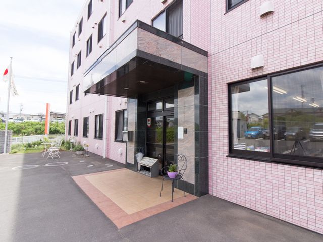 ピンクの壁のエントランス 入口 歓迎感のあるエントランスは、来訪者に明るい第一印象を与えます。窓からは光が入り、開放的で快適な待合スペースが見て取れます。