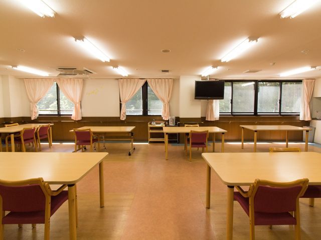広々とした暖かい食堂 食堂 落ち着いた色合いの広々とした食堂で、ご利用者様は毎日の食事をゆっくりとお楽しみいただけます。天井の照明が明るく、窓から自然光が差し込んでいます。