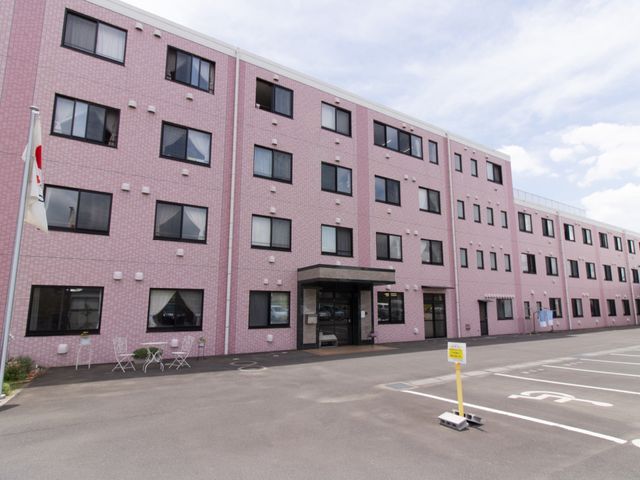 ピンクの壁の建物外観 外観 ゆったりとしたアプローチが特徴的な建物です。この明るく開放的なエントランスでは、新しい職場での一日が始まります。