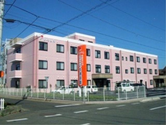 ピンク色の建物外観 施設外観 広々としたピンク色の外観が印象的な、静かな街角に位置する施設です。落ち着いた環境で働くことができそうですね。