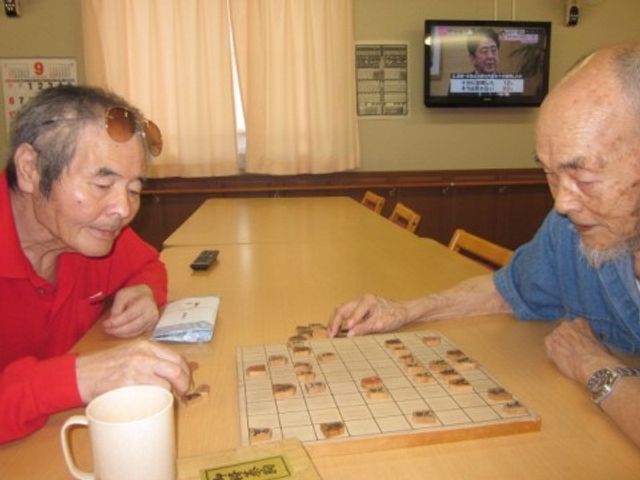 将棋を指す二人のシニア 将棋 ゆったりとした時間を共有する、心地よいコミュニケーションスペースです。お互いの趣味を楽しむ穏やかな様子が印象的です。