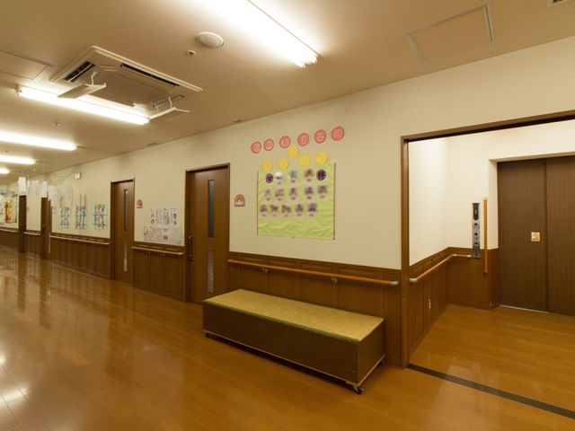 明るい廊下と掲示物 通路 温かみのある木目調で整えられた廊下は、掲示物で色彩豊かに彩られております。ゆとりある空間で快適な移動が可能です。