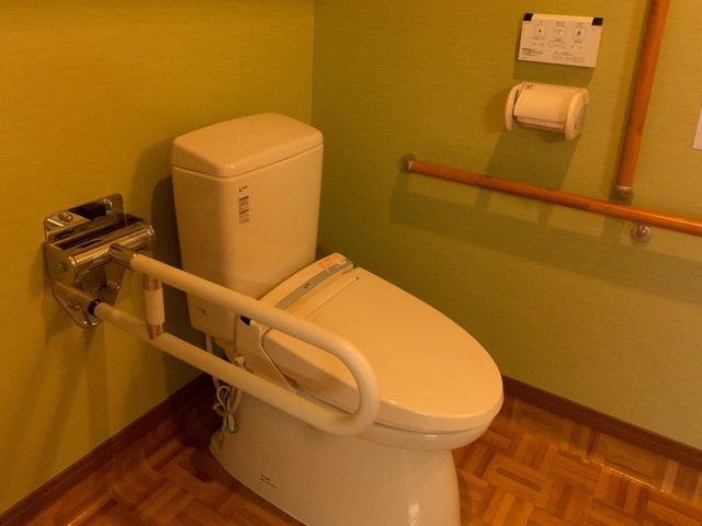 バリアフリートイレ トイレ 安全な手すり付きトイレで、安心してご利用いただけます。床と壁の配色も温かみがあり、快適な空間を提供しています。