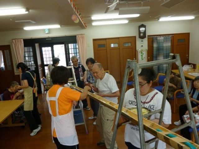 リハビリテーションの活動風景 流しそうめん大会 スタッフが支援する明るい空間で、ご高齢の方々がリハビリに励む様子が見受けられます。利用者の健康維持、生活自立をサポートする職場です。