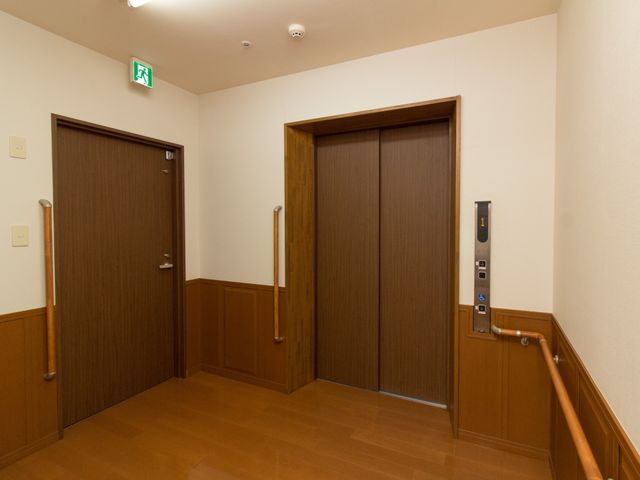 廊下のエレベーター前 エレベーター 手すりが設置された廊下に面したエレベーターです。動線を考慮した設計で、ご利用の方の移動がより快適になっています。