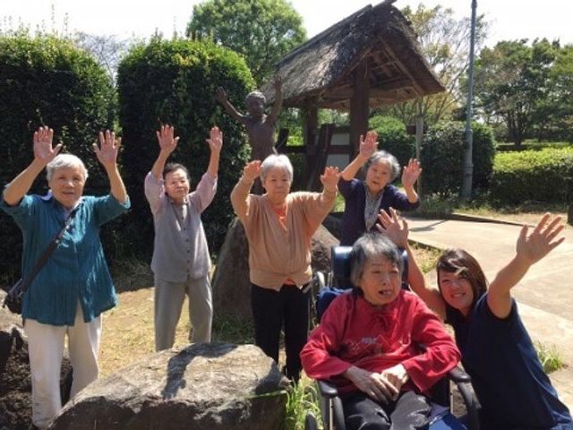 笑顔の集い中庭 だいだらぼう 手を振る利用者様が笑顔で、心温まる中庭でのひとときを過ごされています。明るい陽気の中、共に過ごす時間が豊かな日々を支えます。