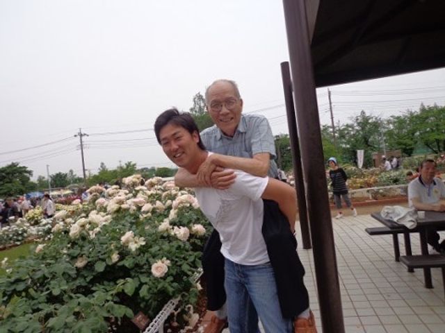 笑顔の二人と花壇 スタッフとご入居者様 広々とした中庭で、明るい笑顔を交わしながら楽しいひと時を過ごしている様子です。安らぎと活気が感じられる環境での就業をご検討ください。
