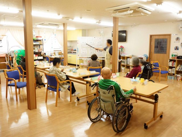明るい共有スペース 共有スペース 椅子が並び、共有のダイニングエリアで利用者がくつろいでいます。スタッフが優しく対応しており、温かい雰囲気が伝わってきます。