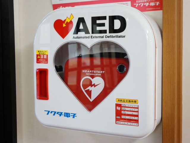 AED設置された壁面 AED ご安心ください、緊急時の心臓救命処置に備えたAEDを設備しています。常に皆様の安全を考え、準備を整えております。