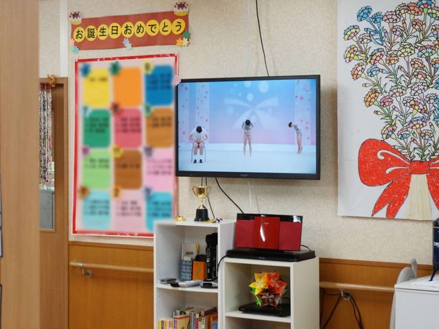 休憩室のテレビと掲示物 リビング カラフルな掲示物が目を引く休憩室で、利用者はくつろぎながら様々な娯楽を楽しむことができます。