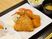 サムネイル 施設の写真 黒い長方形のプレートに1人分の食事がセットされている。白い角皿に3種類のフライが盛られ、複数の野菜が添えられている。