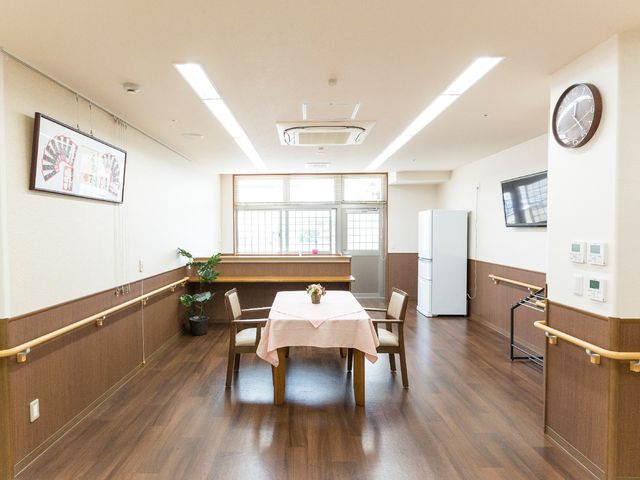 共用スペースの居心地の良さ 喫茶コーナー ゆとりのあるダイニングでは、木目調の床が温かみを感じさせ、親しみやすい雰囲気を演出しています。壁掛けのテレビや大きな時計も備わり、機能的な空間です。