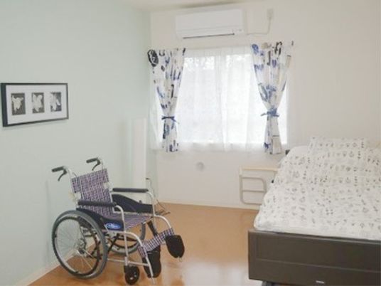 手すりの付いたベッドが設置されている。ベッド横には車椅子が置かれているが、スペースには十分に余裕がある。