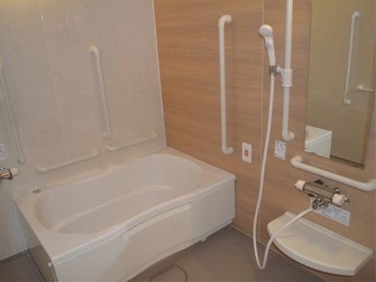 温かみのある木目調の壁が目を惹く清潔感のある浴室である。随所に手すりが設置され、安心して利用していただける。