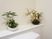 トイレの中は白で統一されて、壁側の空間には白と黒のお皿でおしゃれに配置されている苔と植物が2つ飾ってある。