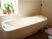 白いタイルの壁と観葉植物が置かれた明るい浴室内。浴槽は大きく、斜めの作りで軽く横になりながら入浴ができる。
