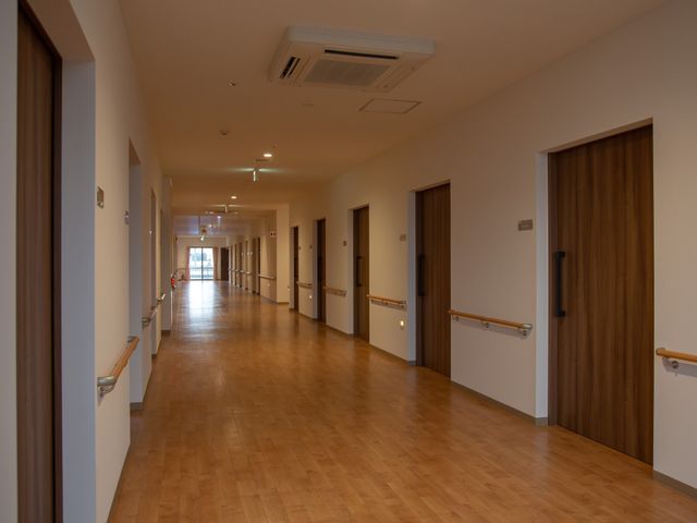 広々とした木目調の廊下 通路 ゆったりとした通路が確保されており、清潔感あふれる木目調の床が印象的です。安全を考慮した手すり設置で、歩行に不安のある方も安心して移動できます。