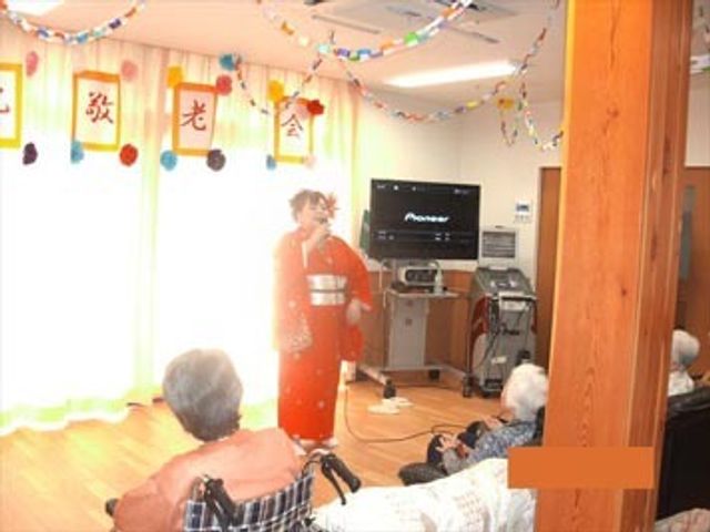 和服姿のパフォーマンス多目的室 イベント 装飾が施された多目的室で、和服を着た人が演出を行っており、利用者はその様子を見守っています。季節の行事を楽しむ場として、心地よい時間が提供されています。