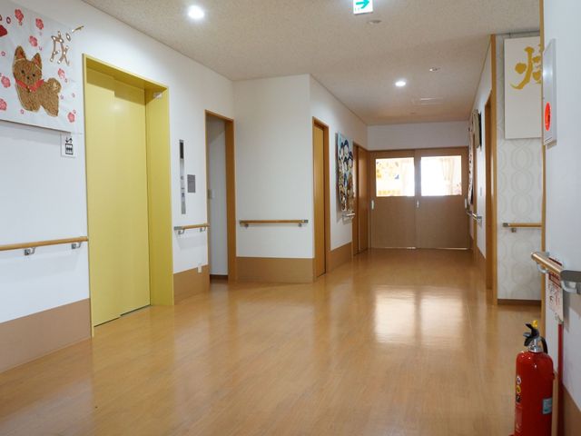広々とした明るい廊下 エレベーターホール 床が木目調で明るい廊下は、壁に飾られたアートがアクセントとなっており、温かみのある雰囲気を演出しております。手すりが整備され、どなたも安心して歩行できる工夫がなされています。