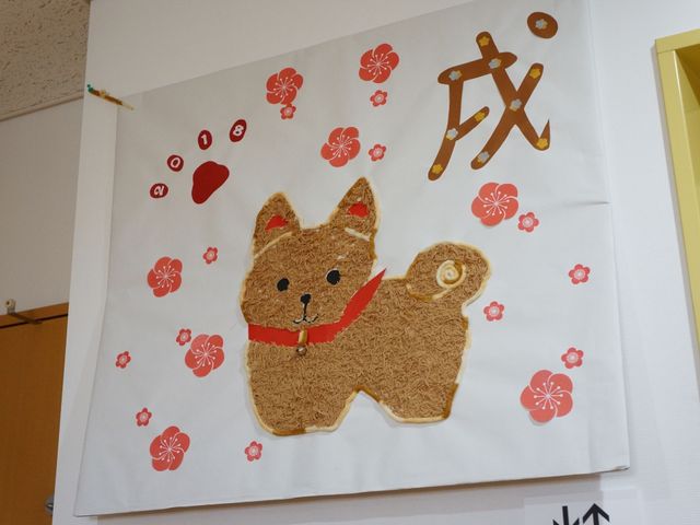 犬の壁飾りと紅白の花 装飾 壁に飾られた犬のモチーフがあたたかな雰囲気を醸し出し、訪れる方々への明るい迎えの意を込めた装飾です。小さなアクセントが、日々の生活に彩りを与えます。