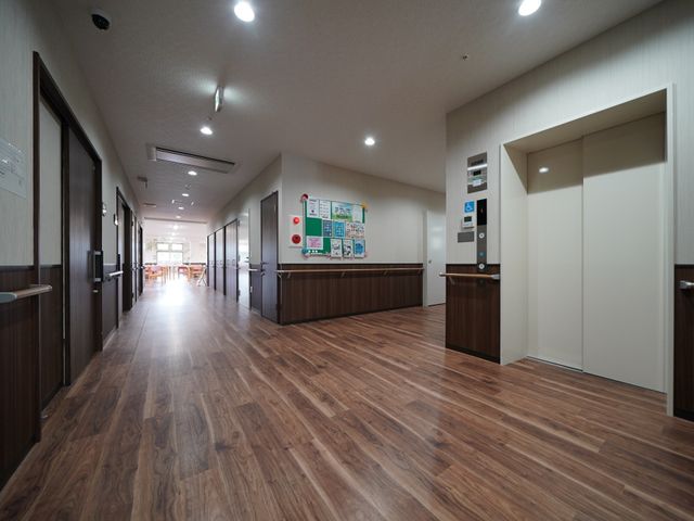 木目調の床の明るい廊下 廊下 清潔感のあふれる広々とした廊下は、日々の業務や利用者様とのコミュニケーションにも適しています。